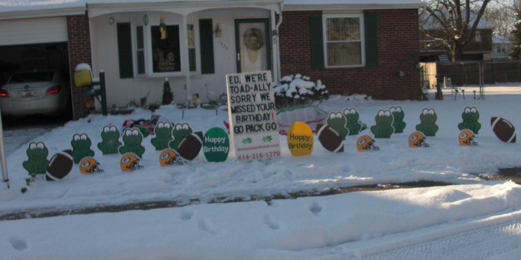 Frog and Green Bay Packers yard signs in snow for Ed's birthday