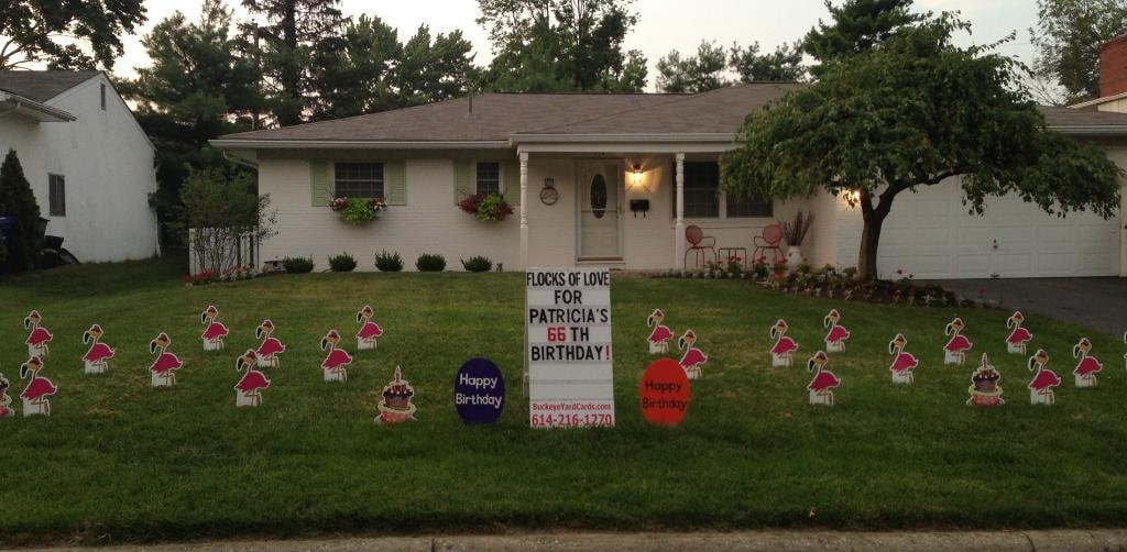 White ranch home at dusk with flamingo yard signs for Patricia's 66th birthday