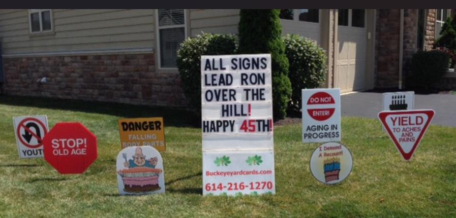 Yard signs reading All Signs Lead Ron Over the Hill Happy 45th