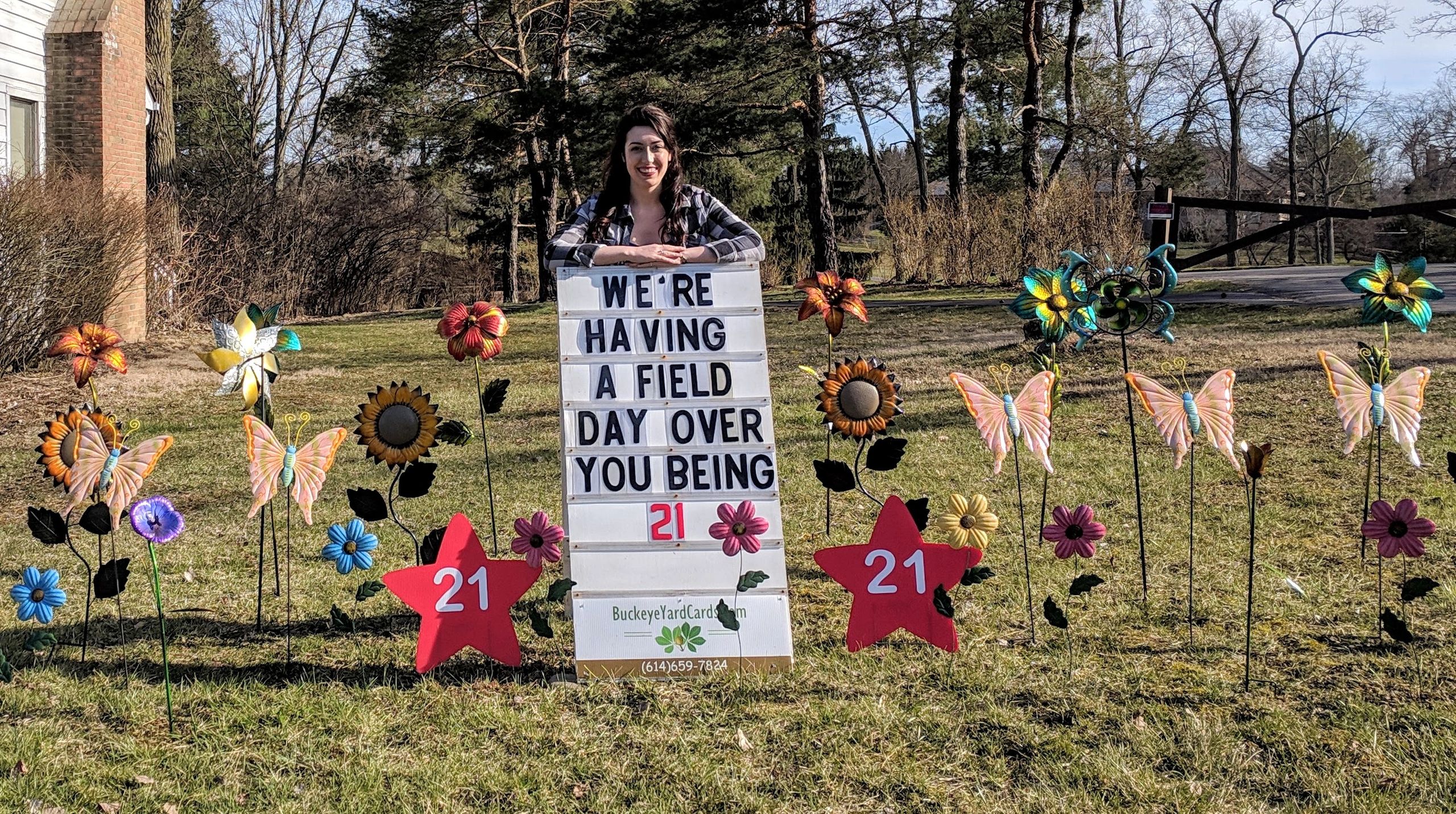 Woman holding sign with colorful butterfly birthday yard display